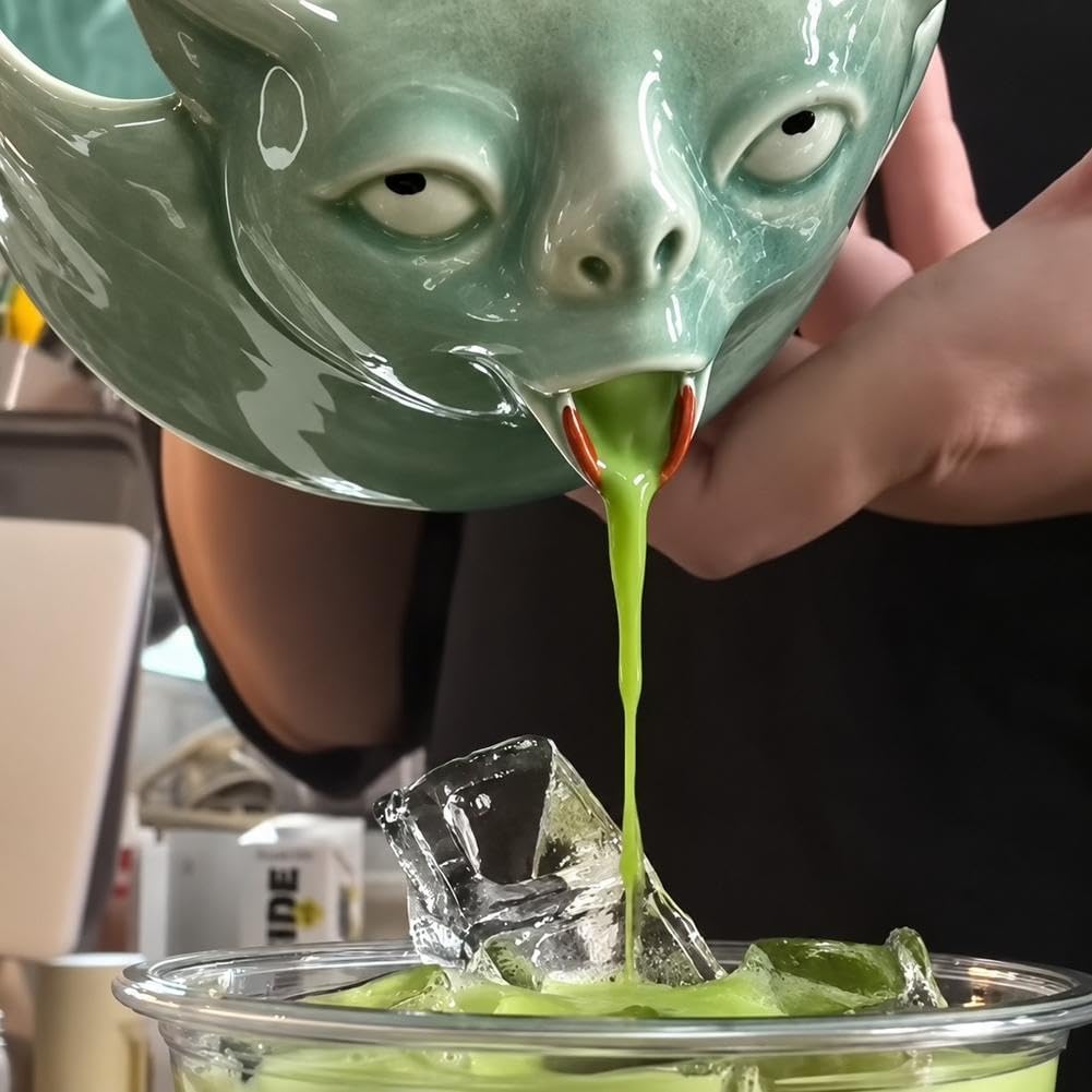 Close up of green matcha pouring from the ceramic cat's mouth into a glass