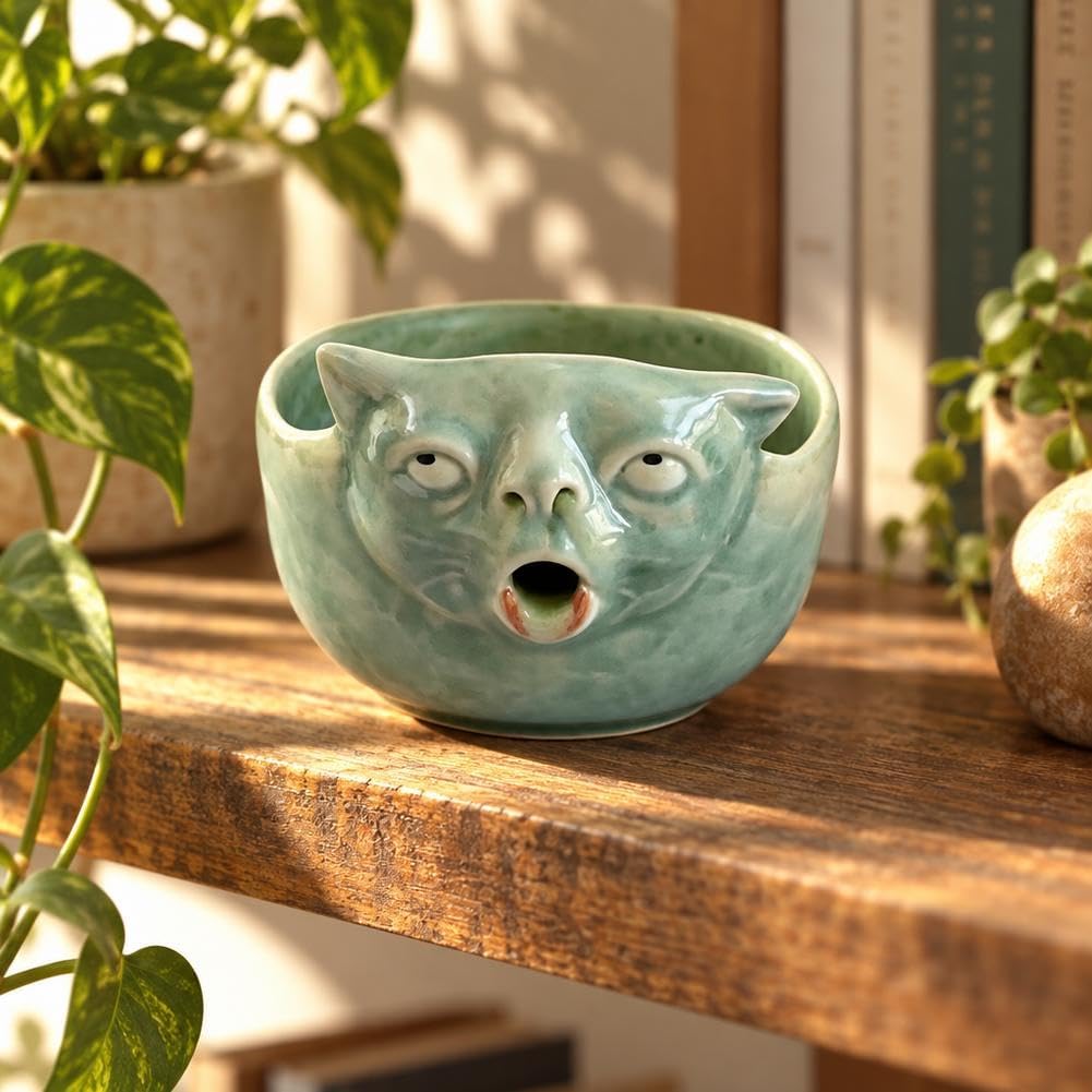 Glossy green ceramic matcha bowl with a funny cat face sitting on a wooden shelf